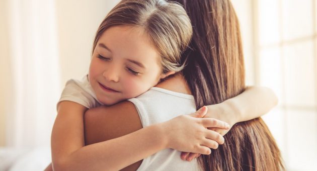 Beautiful young woman and her charming little daughter are hugging and smiling