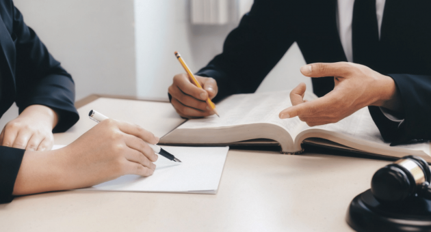 Two professionals in business attire seated at a desk, engaged in discussion with a pen and paper in front of them.