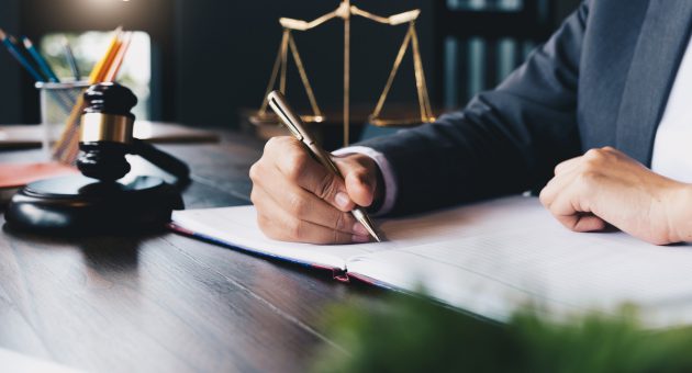 A focused lawyer using a pen to write on paper, with the scales of justice prominently displayed nearby.