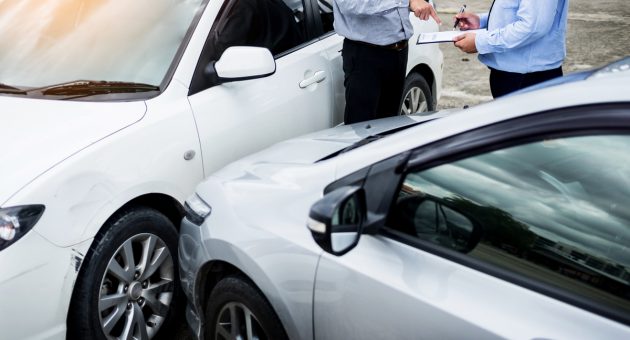 Insurance agent writing on clipboard while examining car after a
